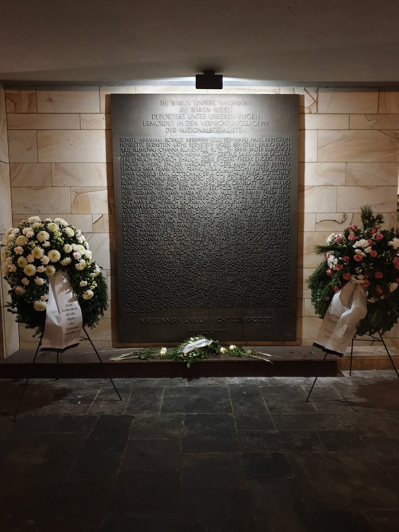 Eine Gedenktafel mit Kränzen und Blumen davor