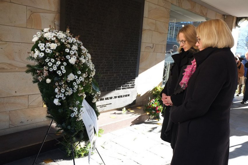 Zwei Frauen vor einem großen Kranz und einer Gedenktafel